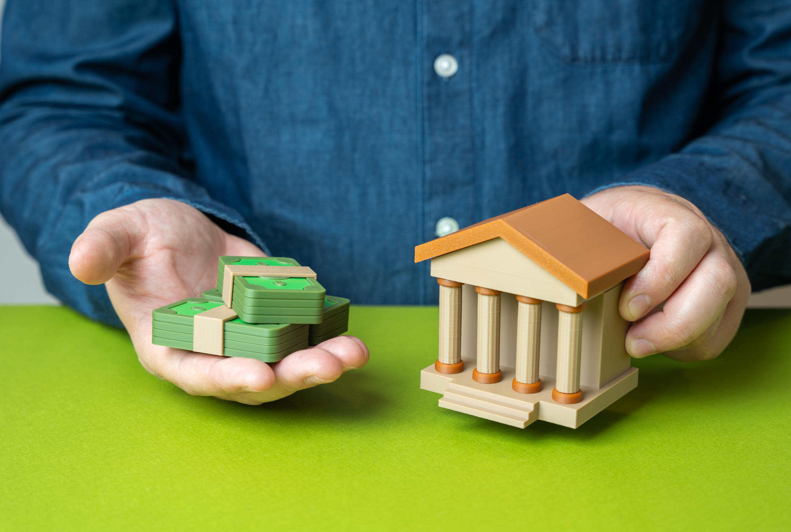 Bank building and stacks of money in a man's hands. Financial literacy. Capital and investments.