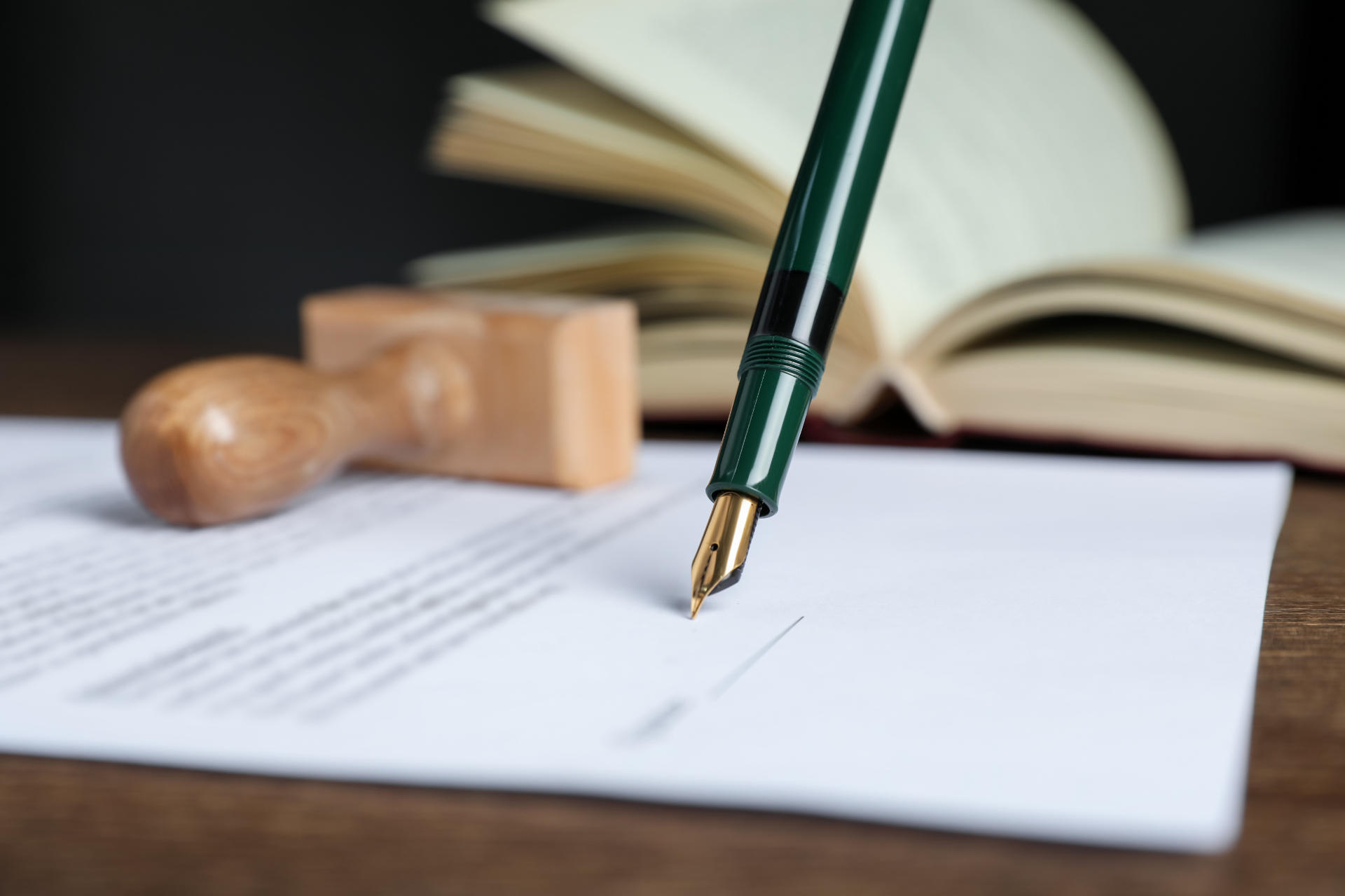 Signing notary document with fountain pen at wooden table agains