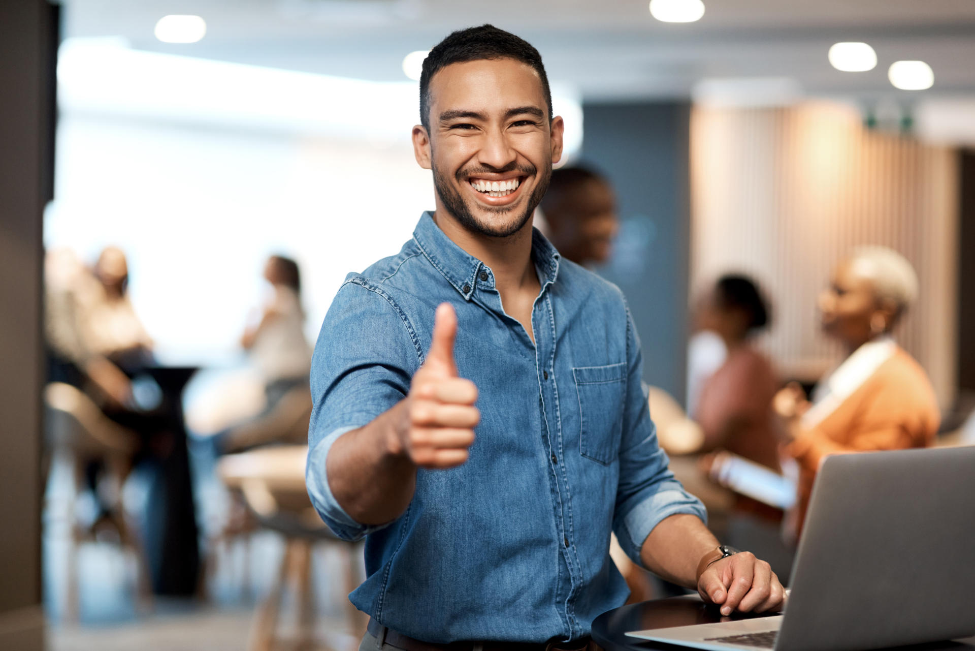 Shot of a young businessman showing thumbs up while using a lapt