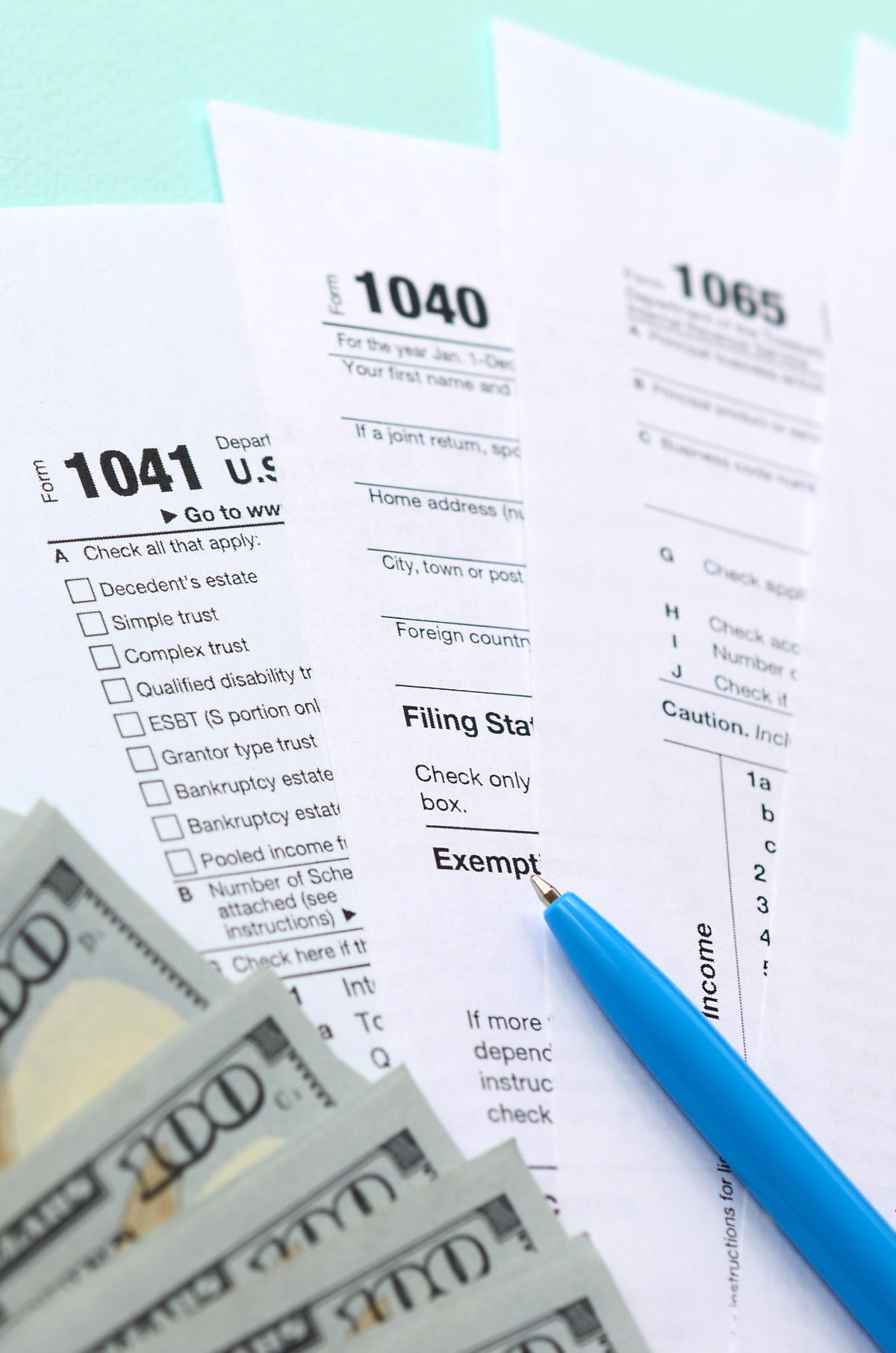Tax forms lies near hundred dollar bills and blue pen on a light blue background. Income tax return
